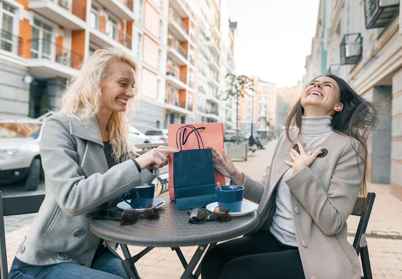Two young beautiful women in an outdoor cafe with shopping bags and cup of coffee.