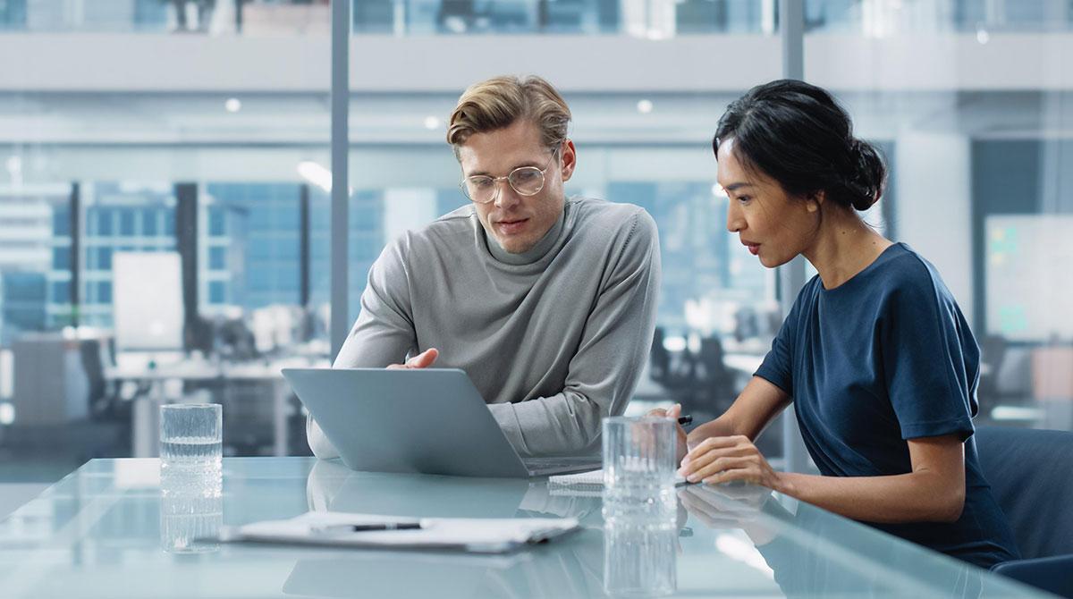 Two business people sitting at a table and looking at a computer.